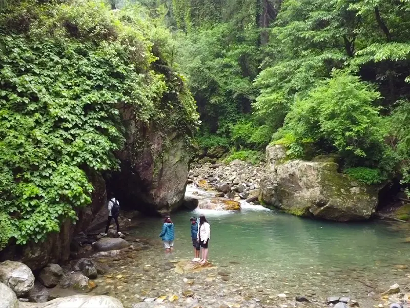 Traveler dipping feet into clear blue pool at Mini Thailand Jibhi
